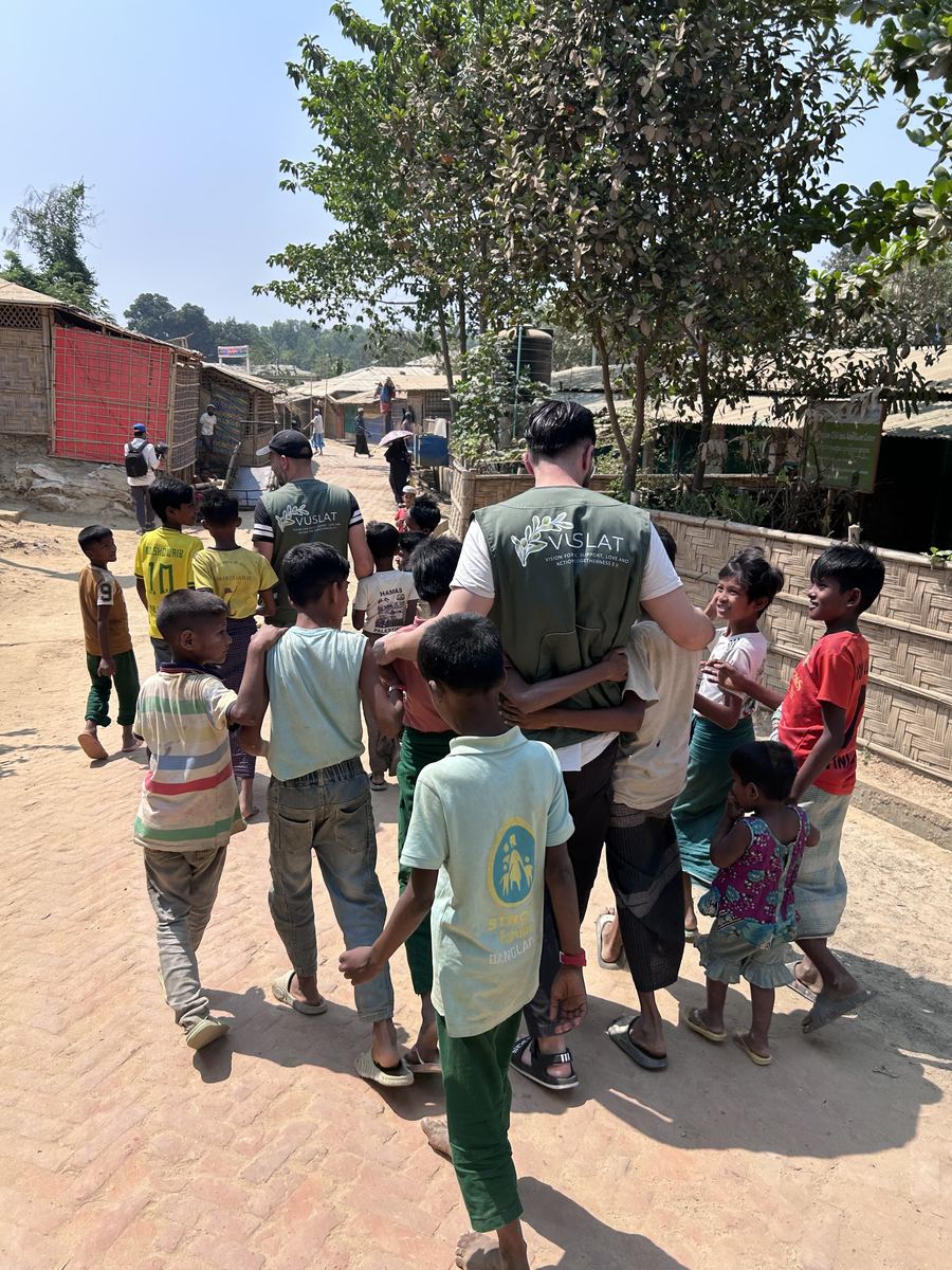 Vuslat-Helfer geht Arm in Arm mit Kindern durch eine Gasse im Rohingya-Camp