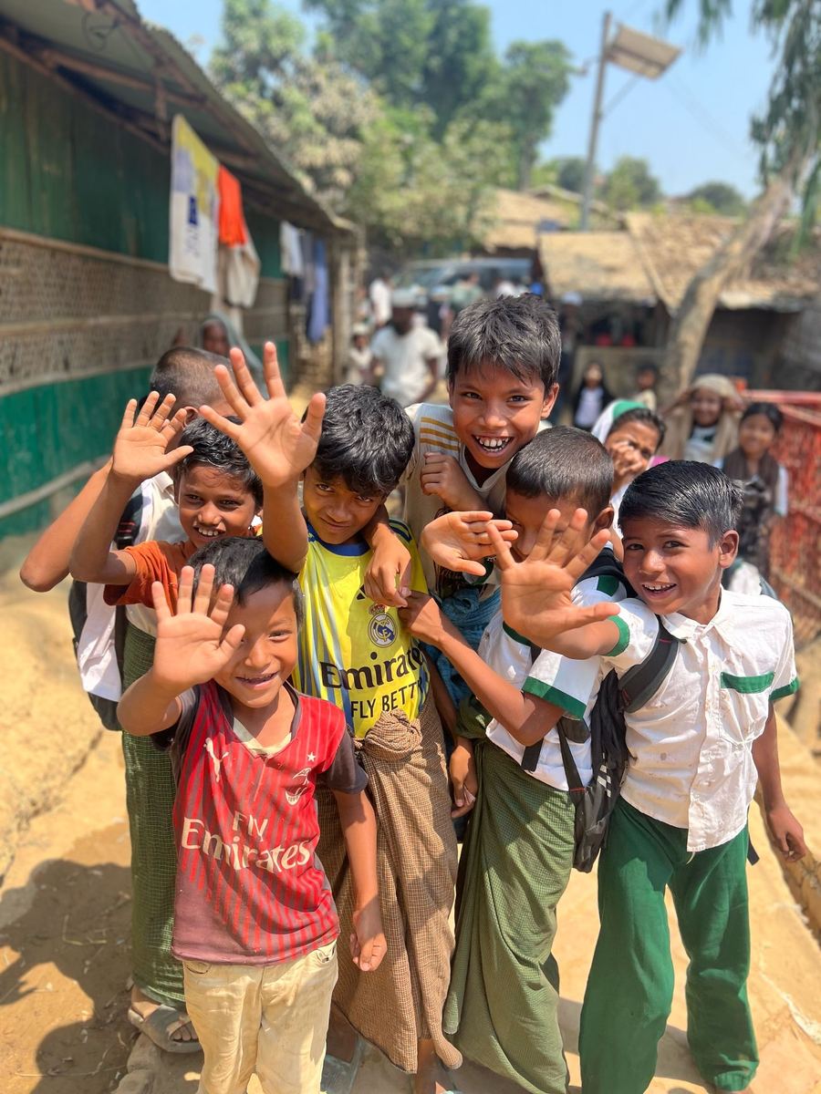 Lachende Kinder winken in einer Gasse des Rohingya-Camps in die Kamera
