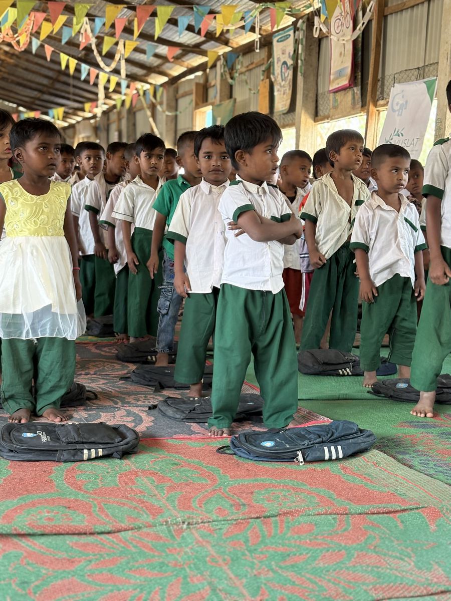 Kinder in Schuluniform stehen in Reihen, vor jedem ein neuer Schulrucksack